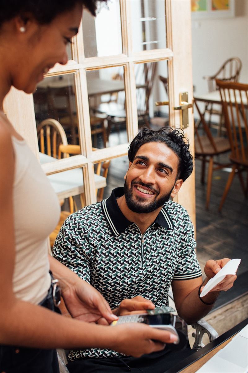 A café customer paying by card while a staff member holds the terminal
